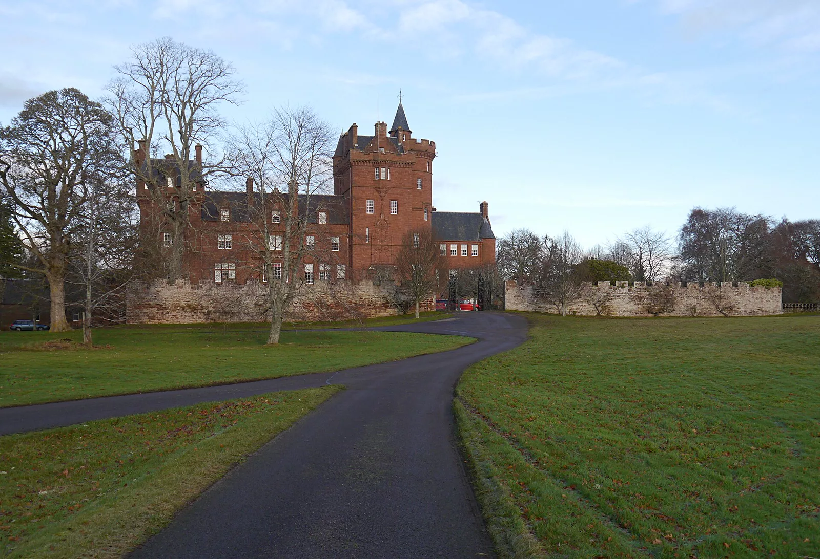 Beaufort Castle, a red sandstone Victorian castle with a corner tower and a crenellated wall, seen across parkland.