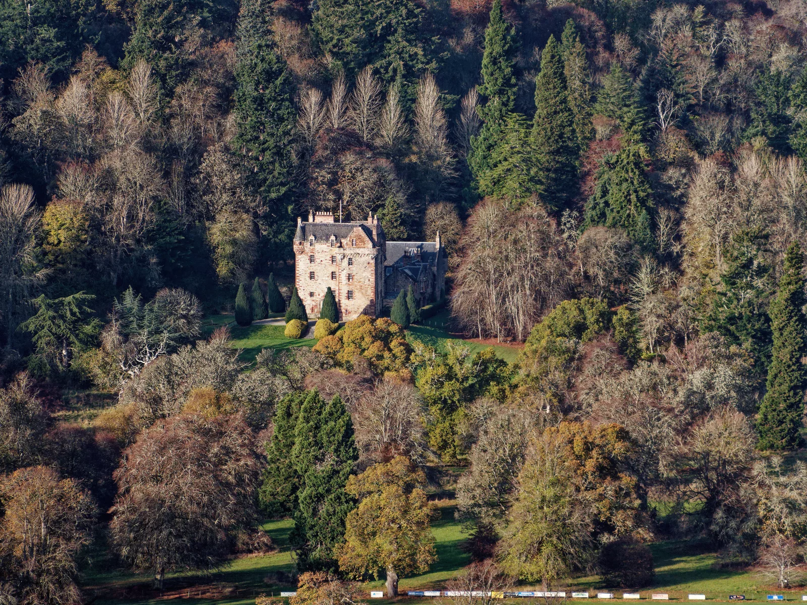 Castle Leod, a tall pink-stone tower house with a slate roof, seen across a lawn with clipped yews and woodland behind.
