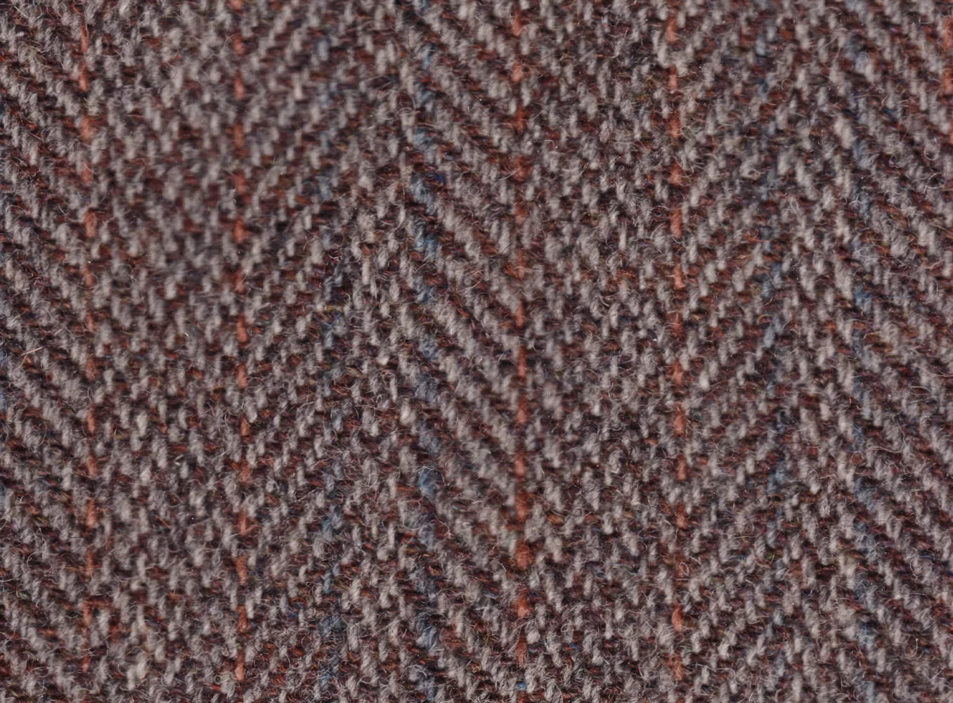 Close-up of brown herringbone tweed, a woven wool cloth, showing the V-shaped twill pattern and flecks of orange and blue yarn.