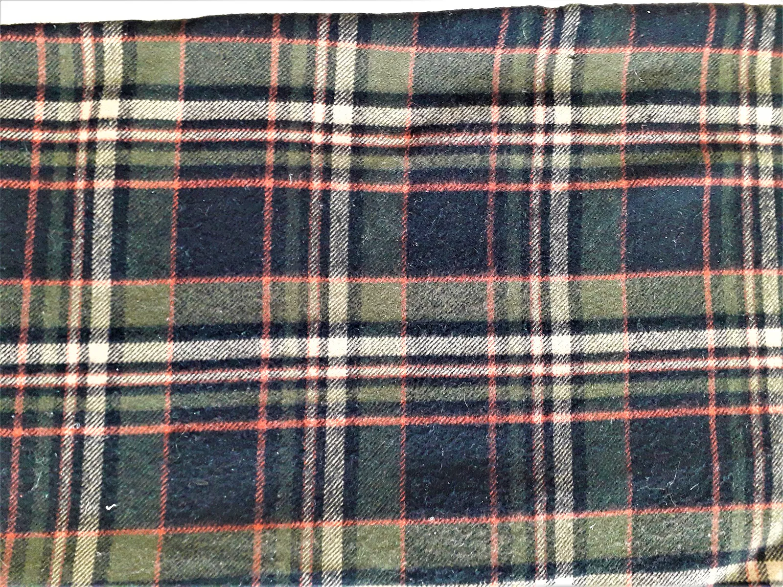 A length of green, navy, black and cream checked twill cloth with thin orange stripes, photographed flat.